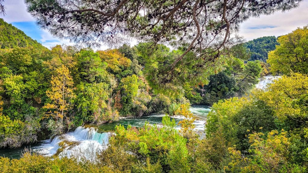 View the river and green landscape at Skradinski Buk with orange clouds. Krka National Park, Croatia: Complete Visitor Guide to Waterfalls, Trails, and TicketsKrka National Park, Croatia: Complete Visitor Guide to Waterfalls, Trails, and Tickets
