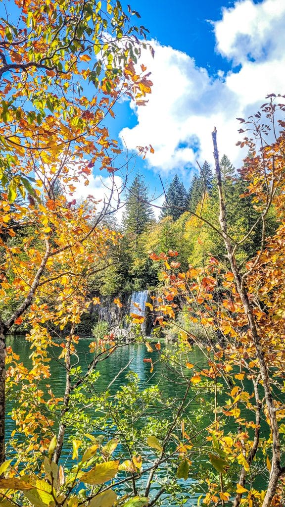 Orange autumn leaves with a waterfall in the background. Visiting Plitvice Lakes: tips, highlights, and where to stay