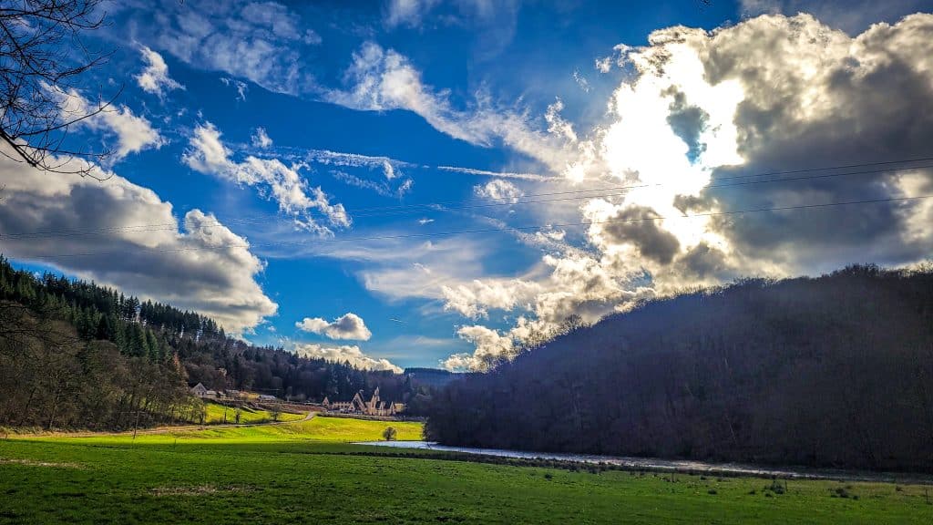 Blue sky with white clouds with a view of a green valley and Abbey Notre-Dame Clairefontaine. Hiking Le Tombeau du Géant in Botassart, Belgium: Trails, tips & local legends