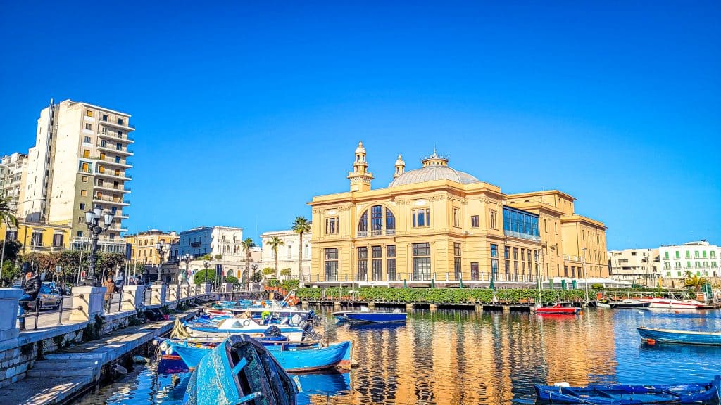 Blue wooden fishing boats and view of Teatro Margherita. Bari Travel Guide: Discover Hidden Gems in Puglia’s Capital. In the worlds jungle travel blog.